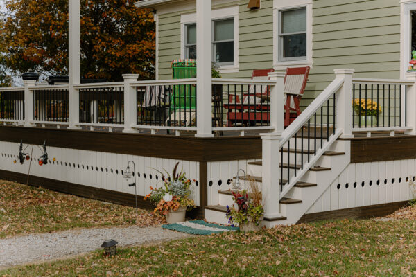 Exterior view of a residential deck with white railings and brown accents, featuring a staircase, potted plants, and seating area, showcasing Knapp Builders' craftsmanship in home construction.