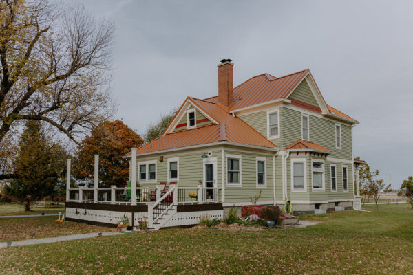 Exterior view of a two-story residential house with a green facade, orange metal roof, and porch, showcasing Knapp Builders' architectural design and craftsmanship.