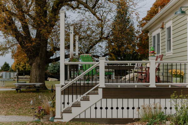 Exterior view of a residential deck featuring white railings, wooden steps, and green chairs, surrounded by autumn foliage and a large tree, showcasing Knapp Builders' craftsmanship in home design.