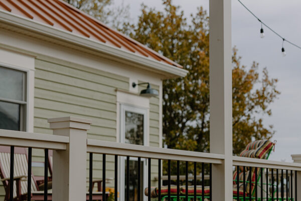 Exterior view of a residential building featuring a green siding, a red metal roof, and a porch railing, with decorative string lights and outdoor seating visible, showcasing Knapp Builders' architectural design.