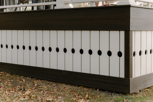 Exterior design detail showcasing a modern building's skirting with alternating white panels and circular cutouts, surrounded by autumn leaves.